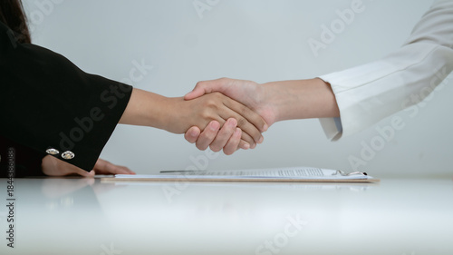 Close up of business handshake over signed document on desk, agreement success, partnership confirmation, trust, deal closing and professional business relationship concept.