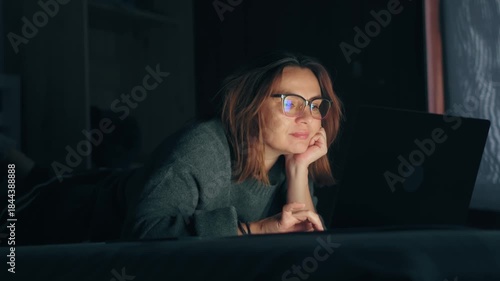 An adult internet addict woman networking concentrated late at night in bed with a laptop