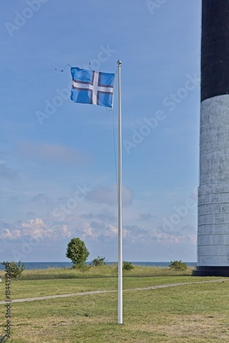 Nordic Estonian flag is flying next to Sörve lighthouse in sunny summer weather, Sõrve Peninsula, Saaremaa, Estonia.
