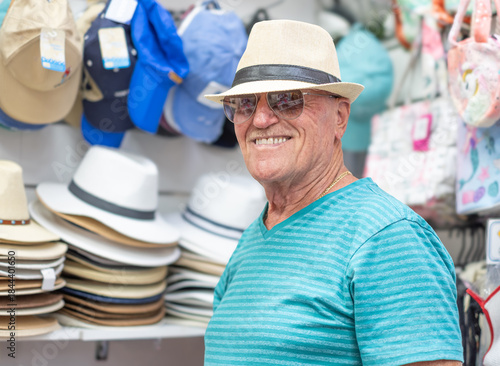 Fotografia A smiling carefree senior man with sunglasses while tries on a hat  shopping in a store