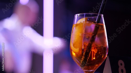 Cocktail in the Spotlight. A Crystal Glass with Citrus and Ice Against a Blurred Ballroom Dance Floor. Couples are dancing in the background against. Slow motion 2x