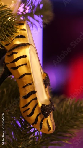 Vertical video footage of a high-Heel Shoe Ornaments on a Christmas Tree Against the Glow of Nightclub Lights. Holiday Elegance