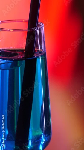 Vertical video footage of a glass of blue cocktail takes center stage. A glass of cocktail against a blurred ballroom dance floor. Couples dancing in the background