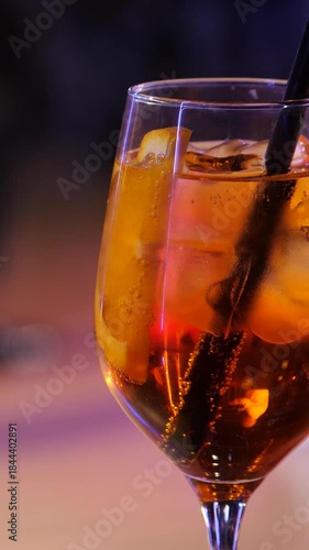 Vertical video footage of a cocktail in crystal Glass with Citrus and Ice Against a Blurred Ballroom Dance Floor. Couples are dancing in the background against. Slow motion 2x