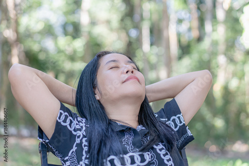 Фотография Pensive middle-aged Asian woman looking upwards, reflecting on nature , close eyes and future thoughts while sitting outdoors