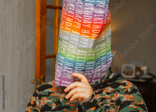 A young boy celebrating his birthday by hiding his face under a bag made from the paper used to wrap his birthday present