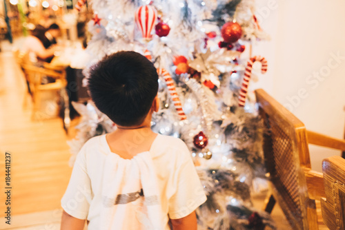 Unrecognizable young boy standing in front of white Christmas tree. Selective focus. Copy space.