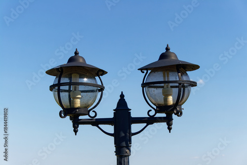 A stylish vintage lamp post with a double-globe design against a clear blue sky.