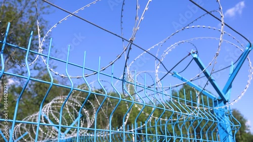 Barbed wire on the metal fence against a blue sky