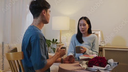 Valentine celebration shows happy young couple sharing romantic love at home, smiling faces show joy with flowers gift box cozy warm light intimate evening.