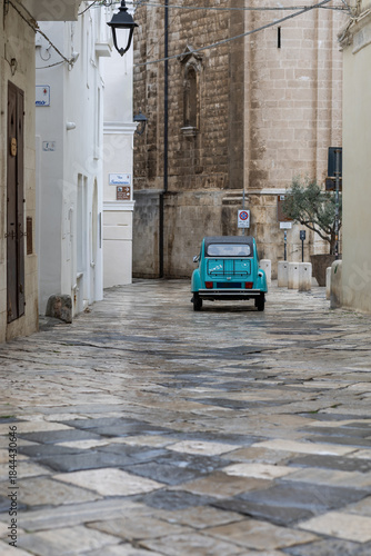 Картината върху платно turquoise car driving away down a wet, narrow cobblestone alley in a historic so