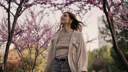 Woman walks under cherry blossom trees in park during springtime with bright sunlight shining on her