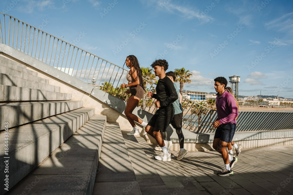 Fototapeta premium A group of three athletes run up the stairs while a male athlete is behind them