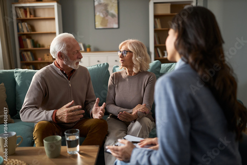 Senior couple talking to each other while having a meeting with insurance agent at home