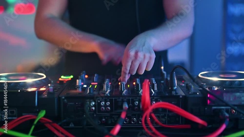 A close-up shot captures the hands of a DJ actively mixing music on a professional turntable controller, scratching a record and adjusting levels during a vibrant party or nightclub event. 
