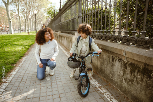 Mother crouched on the ground and smiling while listening to her son riding a bike and talking