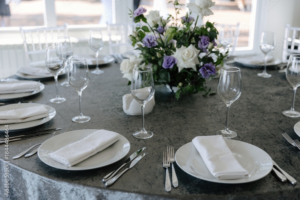 Fototapeta premium Elegant wedding table setting with grey tablecloth, white plates, and purple and white flower centerpiece