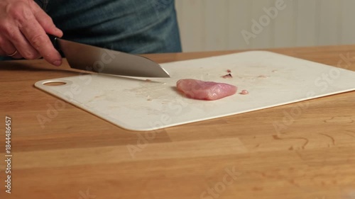 Man butcher cut raw meat with sharp knife at home kitchen. Male person cutting the chicken fillet pieces for cooking. Preparing chopping food. Split poultry breast. Healthy lean meat, low cholesterol