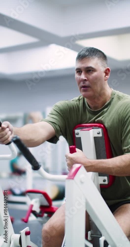 Vertical footage of a middle aged Caucasian man working out in the gym. A focused man works his back muscles intensely using the hammer machine, maintaining strong form throughout his gym session.