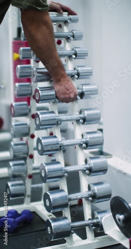 A rack of dumbbells at a gym. A man picks up dumbbells from the rack. Hands close up. A man's hands carefully picking dumbbells from the gym rack, ready to start his workout.