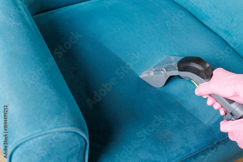 Wet vacuum tool removing stains from blue upholstered armchair seat at home