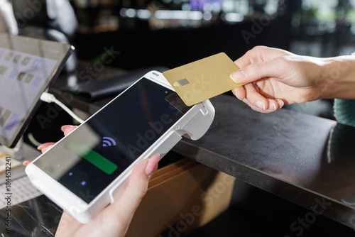 Slika na platnu Contactless NFC card tap on POS terminal at bar counter with laptop and tablet