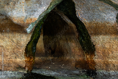 Narrow dark cavity in rock wall formed by long term water erosion and showing layered pattern.