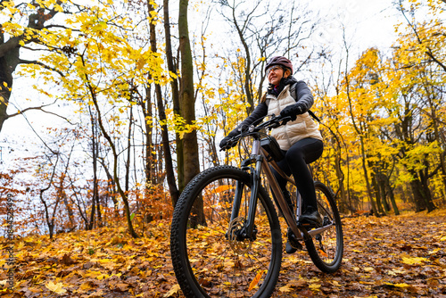 Beautiful middle-aged woman riding bicycle in forest in autumn. Front view