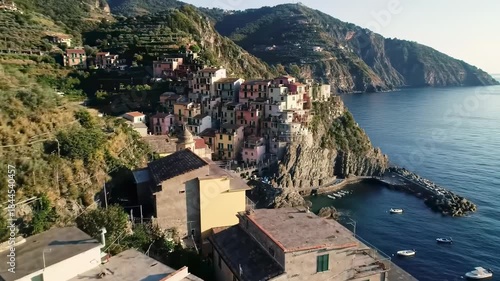 Coastal Italian village clings to rocky cliffs above the deep blue sea, lush green mountains in the background