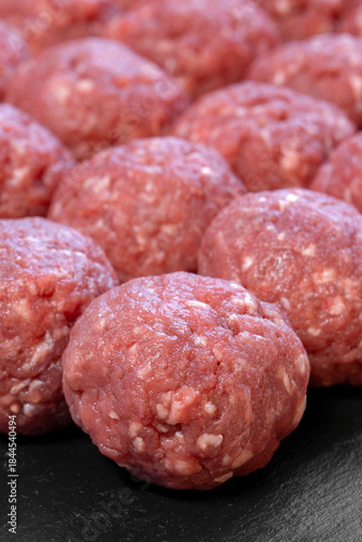 Raw homemade beef meatballs prepared on a black slate cutting board background.