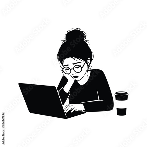 Tired young woman with messy bun and glasses working on laptop with coffee cup nearby