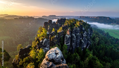 Elevated rocks jut out from a verdant forest, distant hills softened by morning mist, all under a golden sky