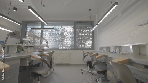 wide dental training classroom with aligned chairs and panoramic window symmetrical benches, overhead linear lights