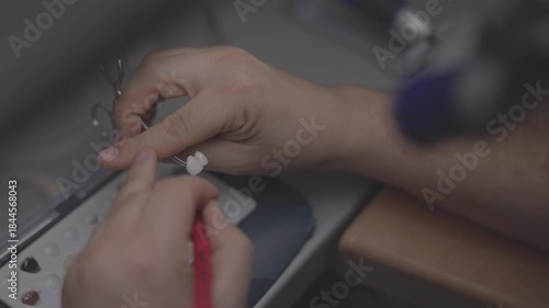 closeup hands adjusting dental bridge with fine tool, technician checks occlusion and contact points on model, careful shaping
