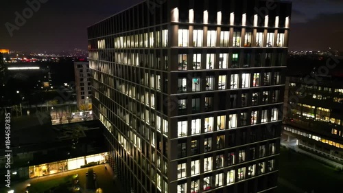 Aerial view of modern architectural building illuminated at night, showcasing vibrant city lights and reflections, with a gradual camera zoom in emphasizing urban design and ambiance