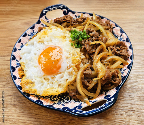 Thai fried egg with stir fried minced pork, sliced onion on top hot white rice in dish on wooden table . Asian food in Thai style and delicious meal on wood background at lunch time.