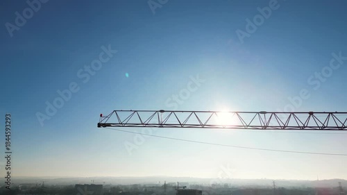 Aerial view of construction crane at building site, capturing the sunlit skyline and urban landscape, showcasing the dynamic movement of the camera as it pans across the scene