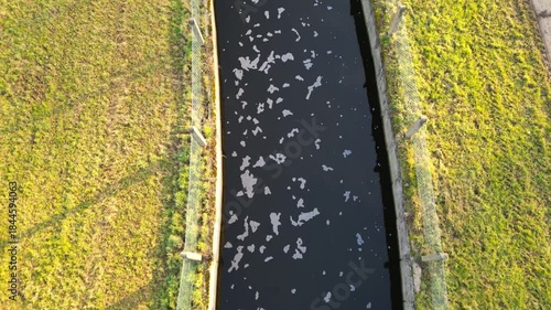 Aerial view of a serene canal bordered by lush green fields and a gravel path, showcasing the tranquil landscape as the camera pans smoothly across the scene