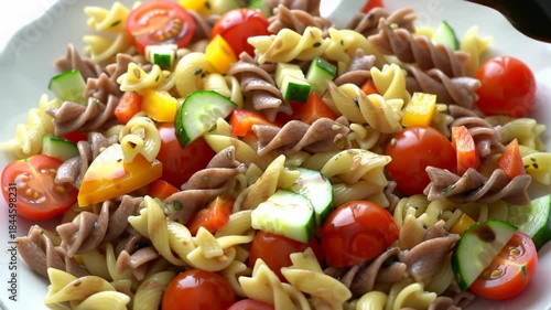 Colorful fusilli pasta salad with tomatoes, cucumbers, peppers and balsamic glaze on a white plate, macro