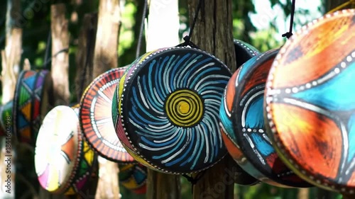 Colorful hand-painted drums hang from wooden posts in outdoor setting, each with unique vibrant geometric designs