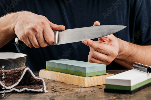 A man sharpens a knife with a grindstone on a rustic wooden table.