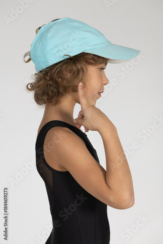 A girl in a tracksuit and a cap poses for a photographer against a white background.
