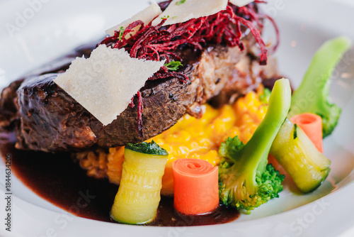 Gourmet plated beef dish with risotto, fresh vegetables, and artistic garnishes in a fine dining restaurant setting