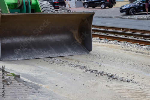 A bulldozer bucket on the road. Rails and asphalt road. Roadworks.