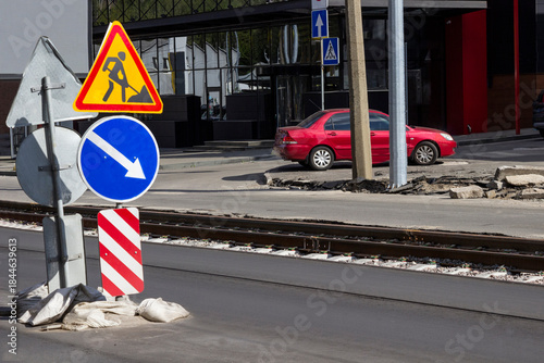 Roadside safety signs during road repairs. Tram track, red car behind lampposts.