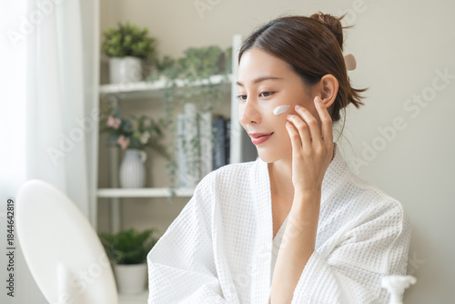 Canvastavla Facial beauty skin care, smile of pretty asian young woman in bathrobe looking at mirror, hand applying moisturizer lotion on her face, putting cream treatment before makeup cosmetic routine at home
