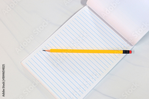 Yellow pencil on lined notebook in flat lay style. Minimal and clean composition with copy space. Concept for education, writing, note taking, and workspace background