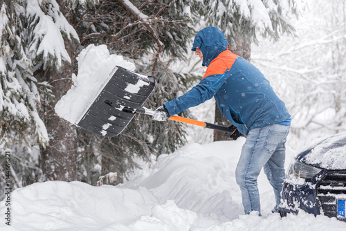 Clearing snow from a car stuck in a snowdrift using a shovel.