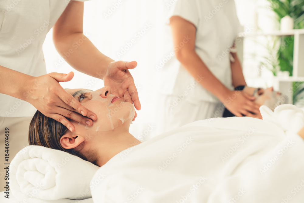Obraz premium Serene modern daylight ambiance of spa salon, couple customer indulges in rejuvenating with facial skincare mask. Facial skin treatment and beauty cosmetology procedure for face. Quiescent