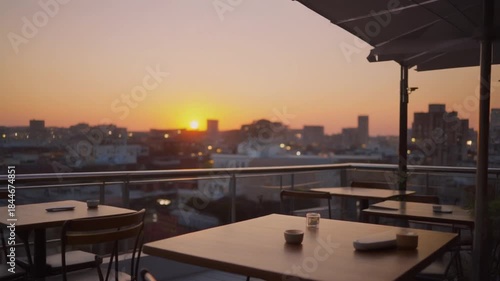 A serene rooftop restaurant patio with tables and chairs overlooking a city skyline during a warm sunset 